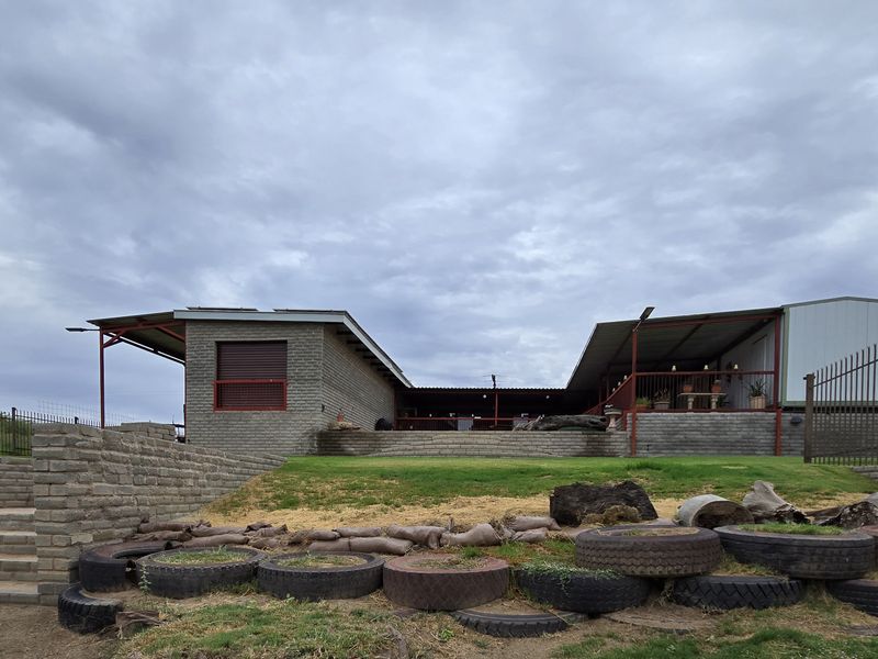Rear view of the property featuring brick construction, a covered patio area, and tiered landscaping with retaining walls and security fencing.