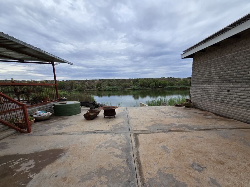 An expansive outdoor patio area featuring concrete flooring and a metal roof structure, overlooking a scenic waterfront landscape.