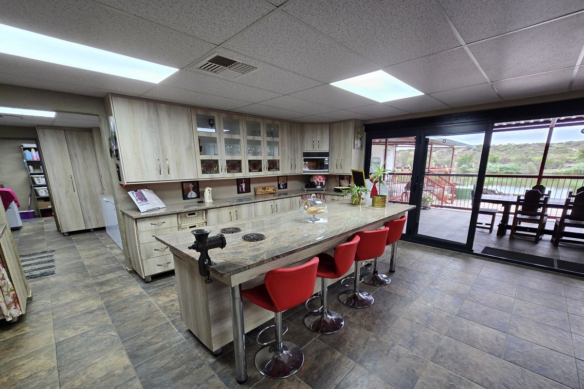 Spacious kitchen featuring light wood cabinetry, a large stone-topped island, tiled flooring, and direct access to an outdoor patio area.