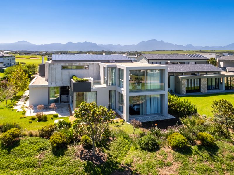 Aerial view of a modern multi-level residence featuring concrete architecture, expansive glass windows, and a well-maintained landscaped garden with mountain views.