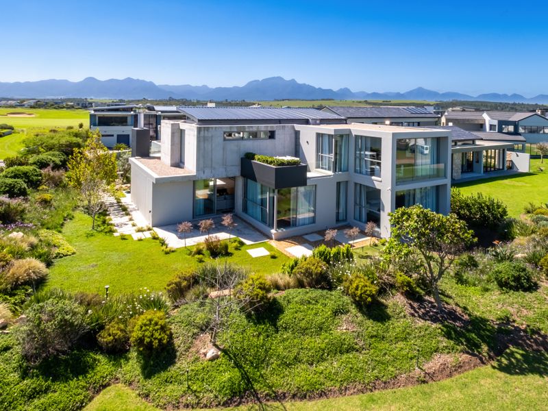 Aerial view of a modern multi-story residence featuring concrete architecture, expansive glass windows, and a well-maintained landscaped garden in a scenic estate setting.