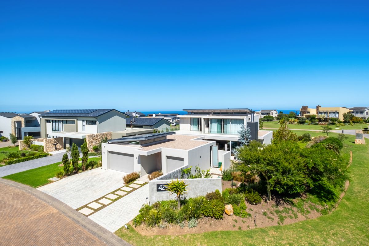 Aerial view of a modern residential property featuring a double garage, paved driveway, solar panels, and well-maintained landscaped gardens in a coastal estate setting.