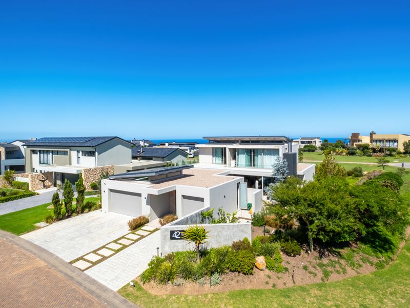 Aerial view of a modern residential property featuring a double garage, paved driveway, solar panels, and well-maintained landscaped gardens in a coastal estate setting.