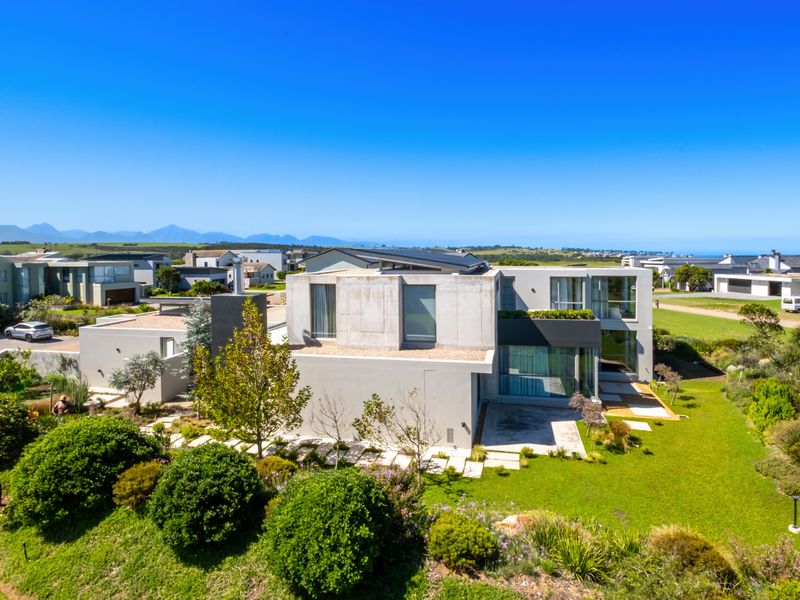 Aerial view of a modern contemporary house featuring concrete architecture, large glass windows, and a well-maintained landscaped garden in a coastal estate setting.