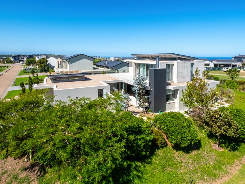 Aerial view of a modern architectural house featuring a flat roof, concrete exterior elements, and landscaped grounds in a coastal estate setting.