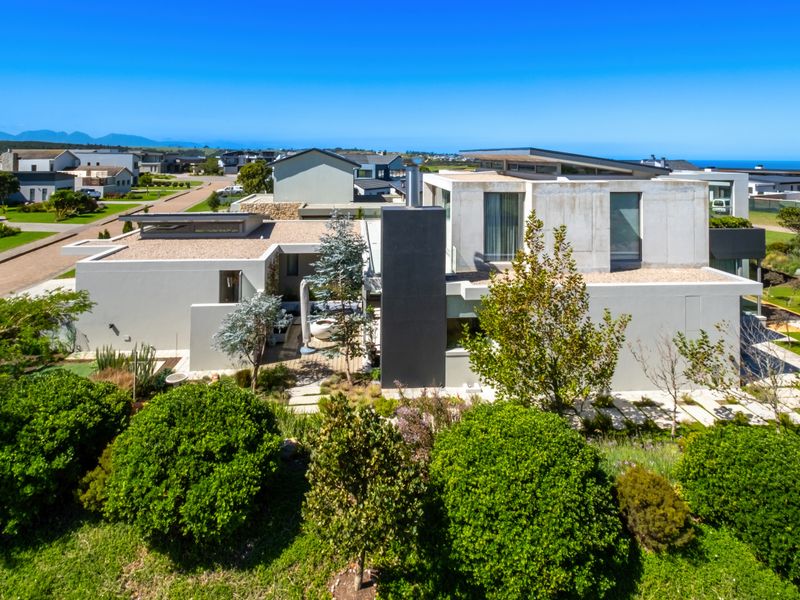 Aerial view of a modern architectural house featuring a flat roof, concrete exterior walls, and a well-maintained landscaped garden in a coastal estate setting.