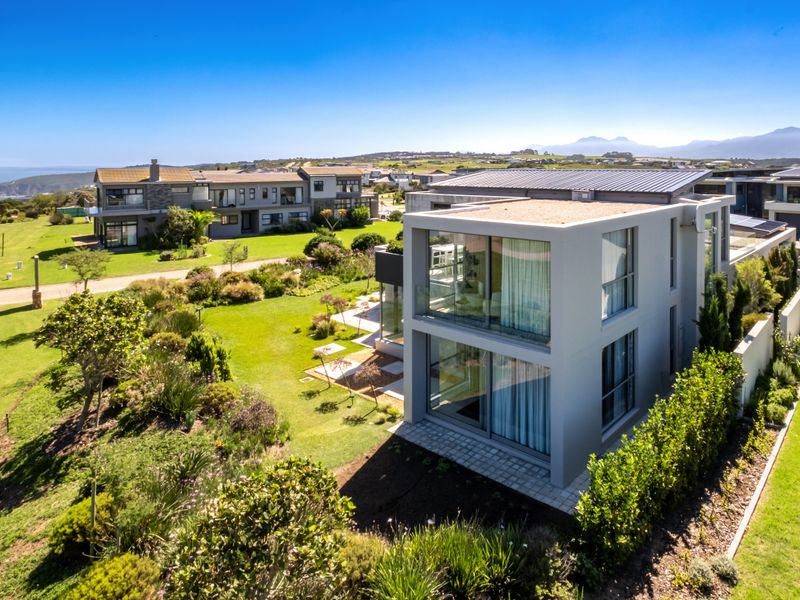Aerial view of a modern two-story residential property featuring clean architectural lines, large glass sliding doors, and a well-maintained landscaped garden in a coastal estate.