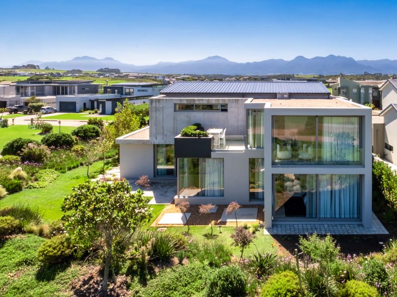 Aerial view of a modern multi-story residential property featuring concrete architecture, large glass windows, and a well-maintained landscaped garden in a scenic estate.
