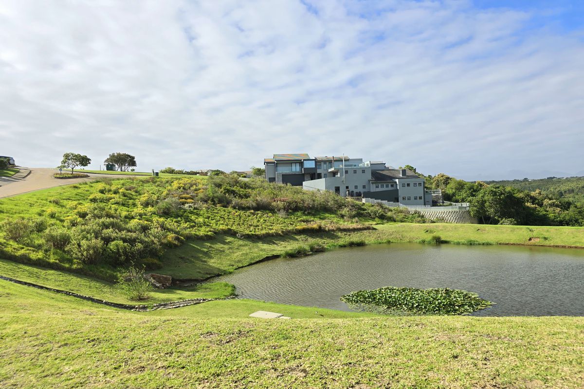 A scenic view of a residential plot featuring a natural pond, landscaped grass slopes, and surrounding estate architecture.