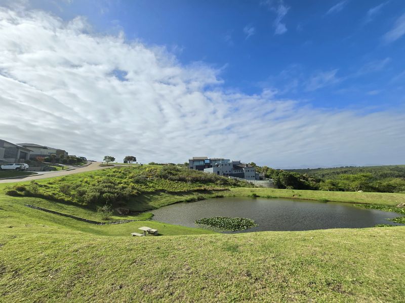 A scenic view of a landscaped residential estate featuring a central pond, manicured lawns, and surrounding natural vegetation.