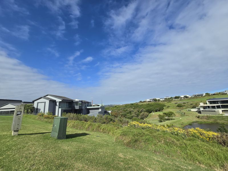 A scenic view of a residential estate landscape featuring rolling green hills, natural vegetation, and nearby modern architectural homes.