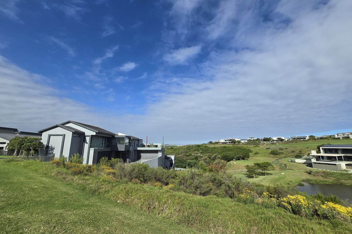 A scenic view of the residential estate, featuring landscaped green spaces, a natural pond, and surrounding modern architectural homes under a clear sky.