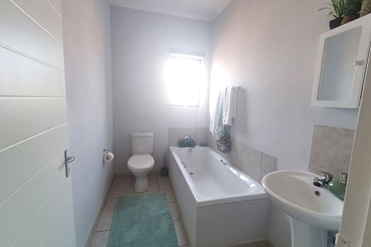 A functional bathroom featuring a bathtub, pedestal basin, and toilet with neutral tiled flooring and splashbacks.