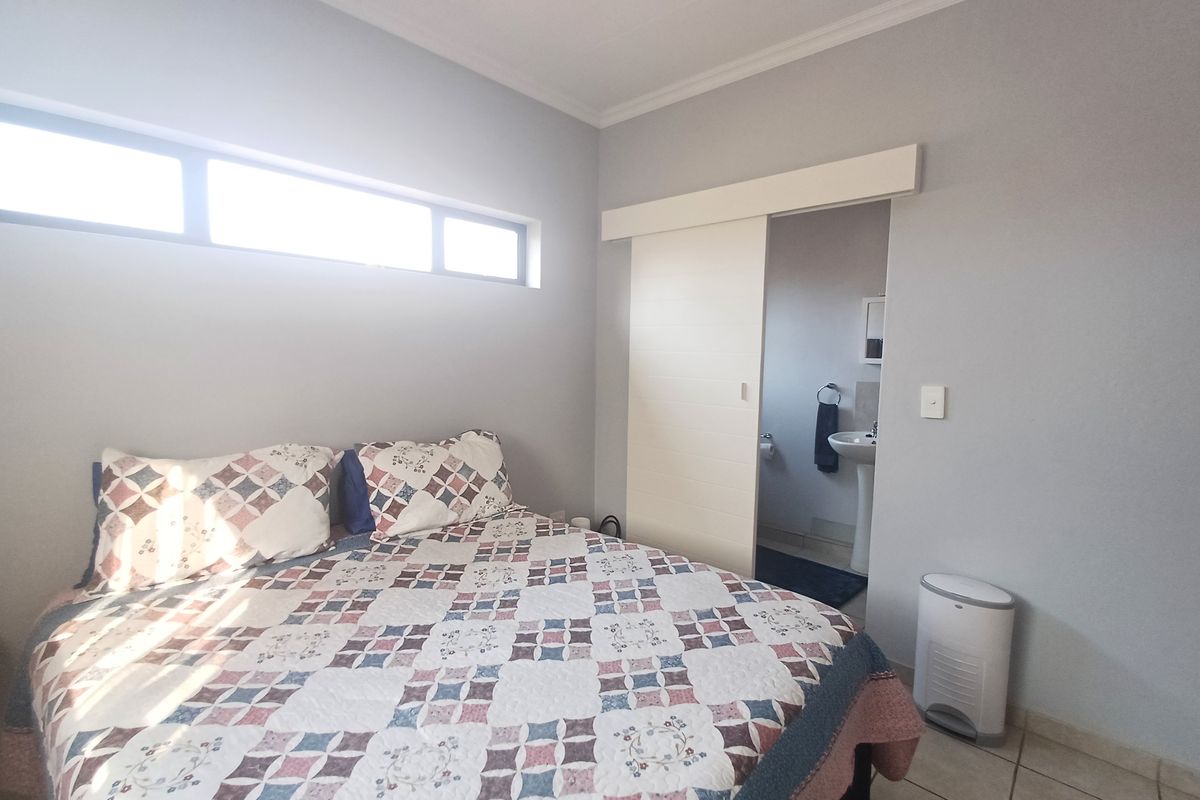 A well-lit bedroom featuring clerestory windows, tiled flooring, and a sliding door providing direct access to an en-suite bathroom.