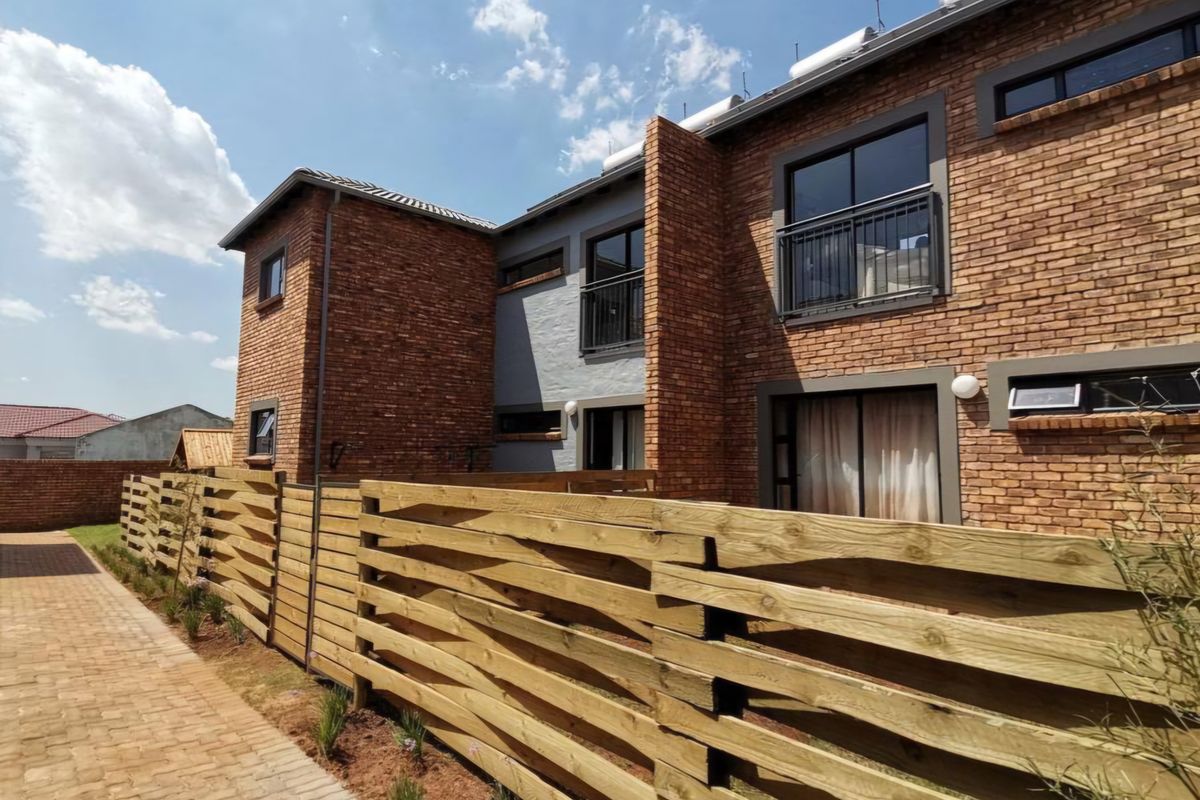 Rear view of a modern face brick apartment complex featuring timber slat fencing, paved walkways, and balcony access.