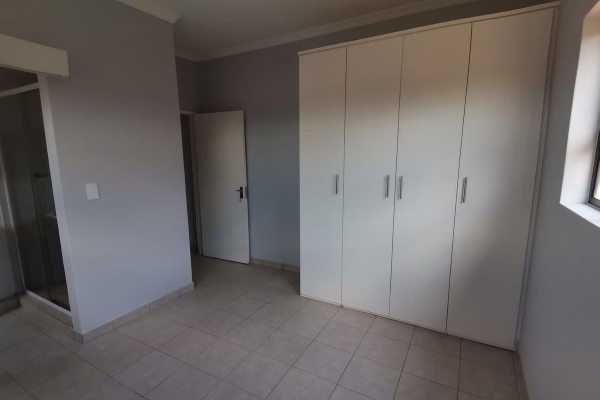 A clean, empty bedroom featuring neutral grey walls, tiled flooring, and ample built-in cupboard storage with direct access to an en-suite bathroom.