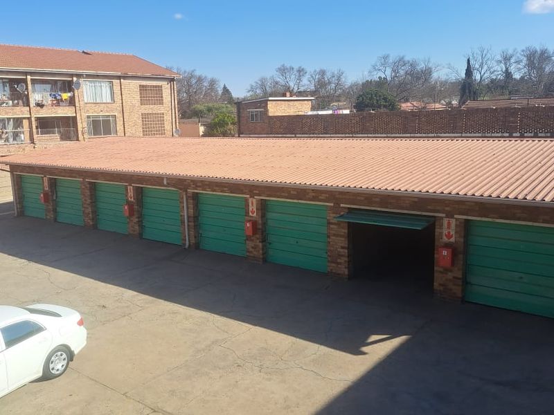 A row of brick-built garages with corrugated metal roofing, featuring green roll-up doors and fire extinguishers mounted on the exterior pillars.