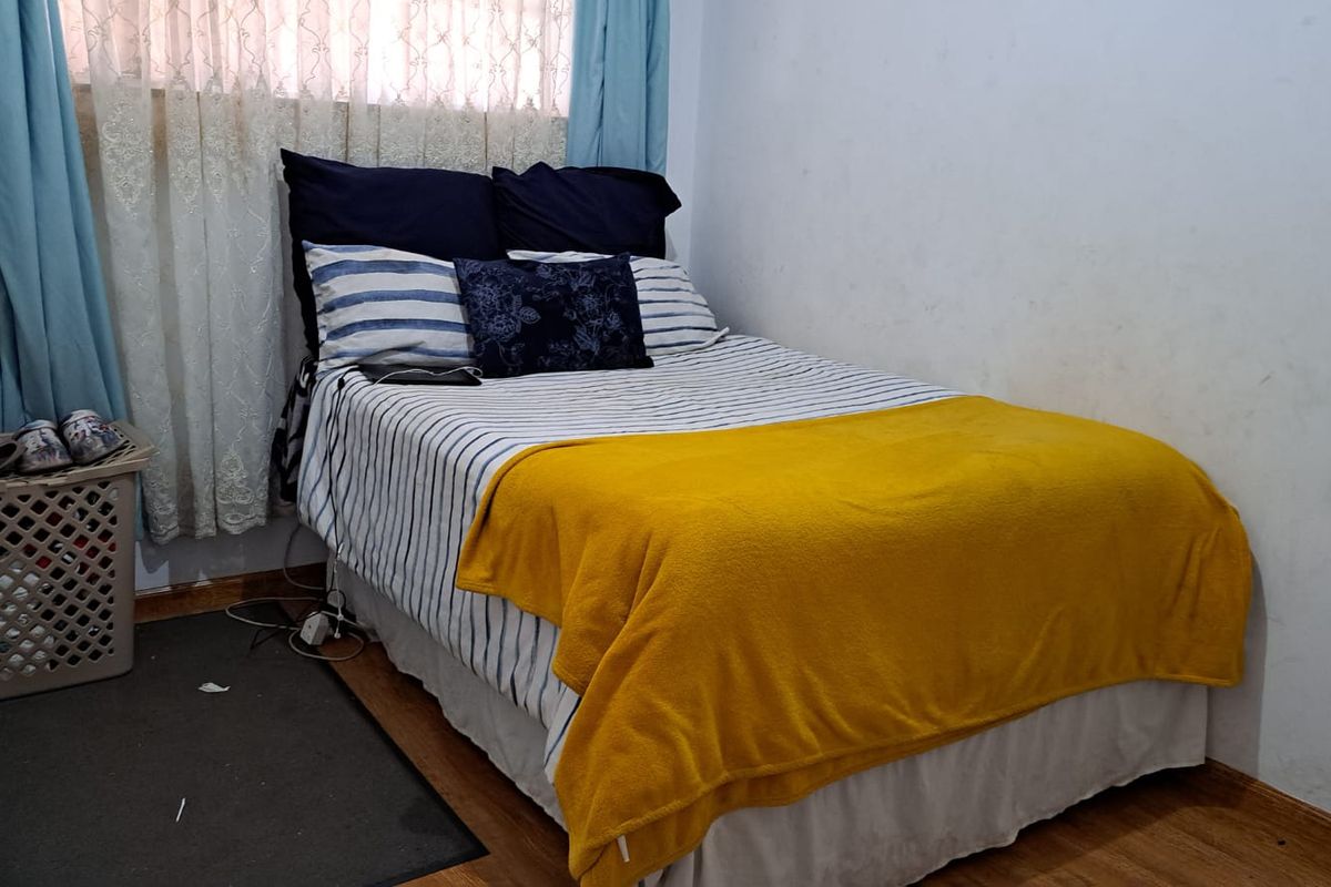 A compact bedroom featuring laminate flooring and a window with curtains.