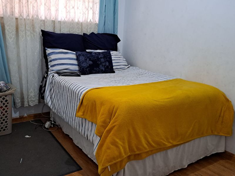 A compact bedroom featuring laminate flooring and a window with curtains.