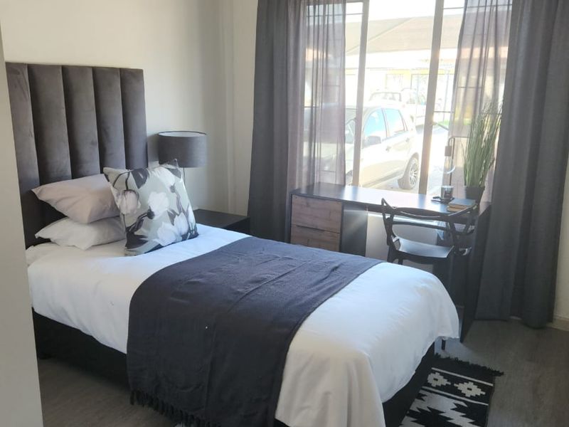 A well-lit bedroom featuring neutral wall tones, laminate flooring, and a large window with curtain tracks, providing a comfortable and functional living space.