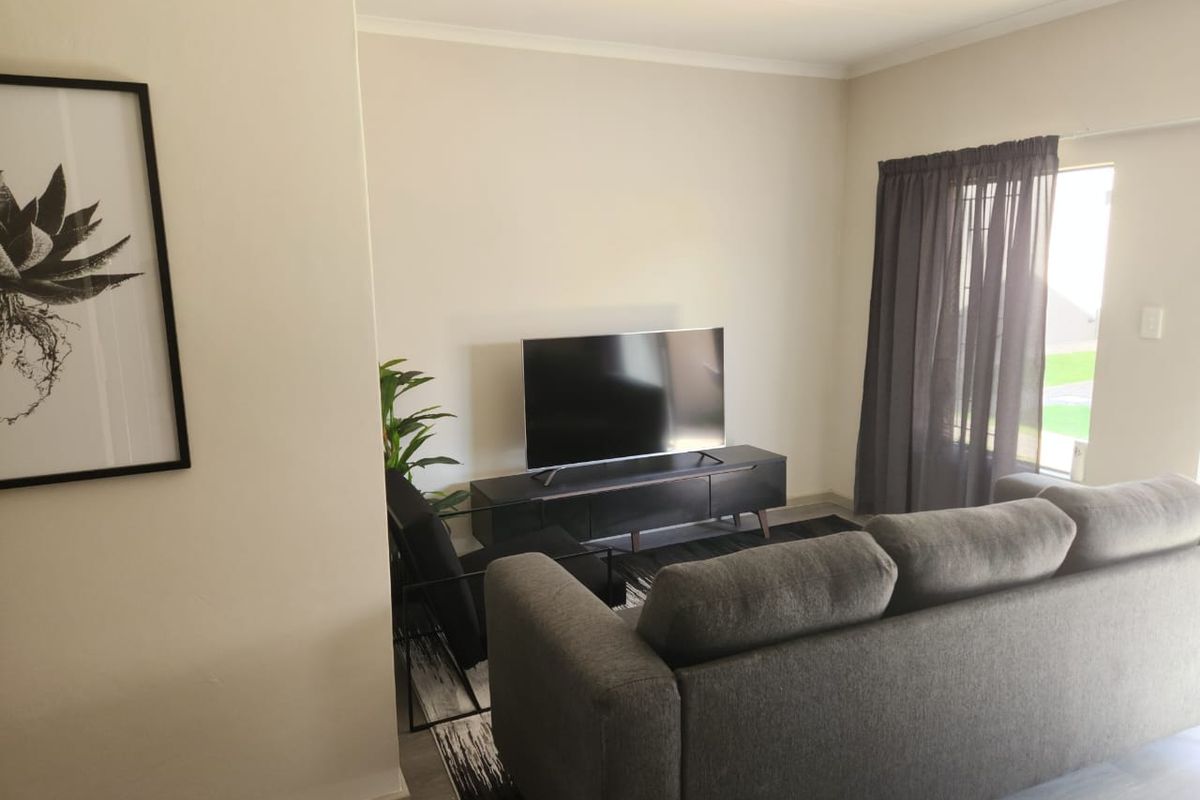 A well-maintained living room featuring neutral wall finishes, natural light through a window with curtain tracks, and standard electrical fixtures.