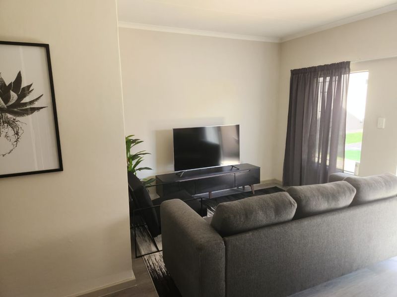 A well-maintained living room featuring neutral wall finishes, natural light through a window with curtain tracks, and standard electrical fixtures.