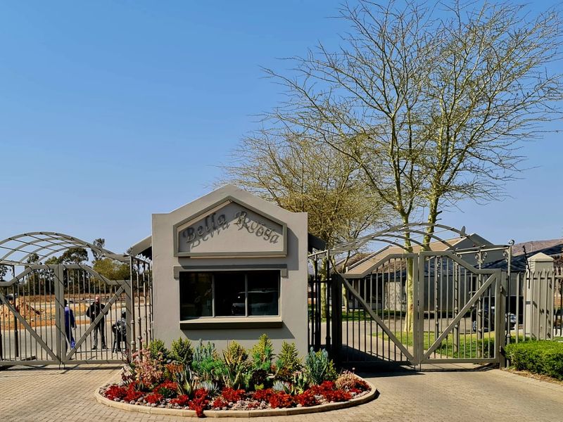 The secure entrance gate and guard house of the Bella Rosa estate, featuring paved access and well-maintained landscaped garden beds.