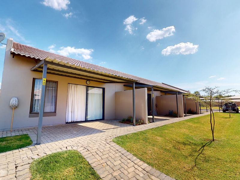 Rear view of a residential unit featuring a paved patio area, covered walkway, and sliding glass doors leading into the home.