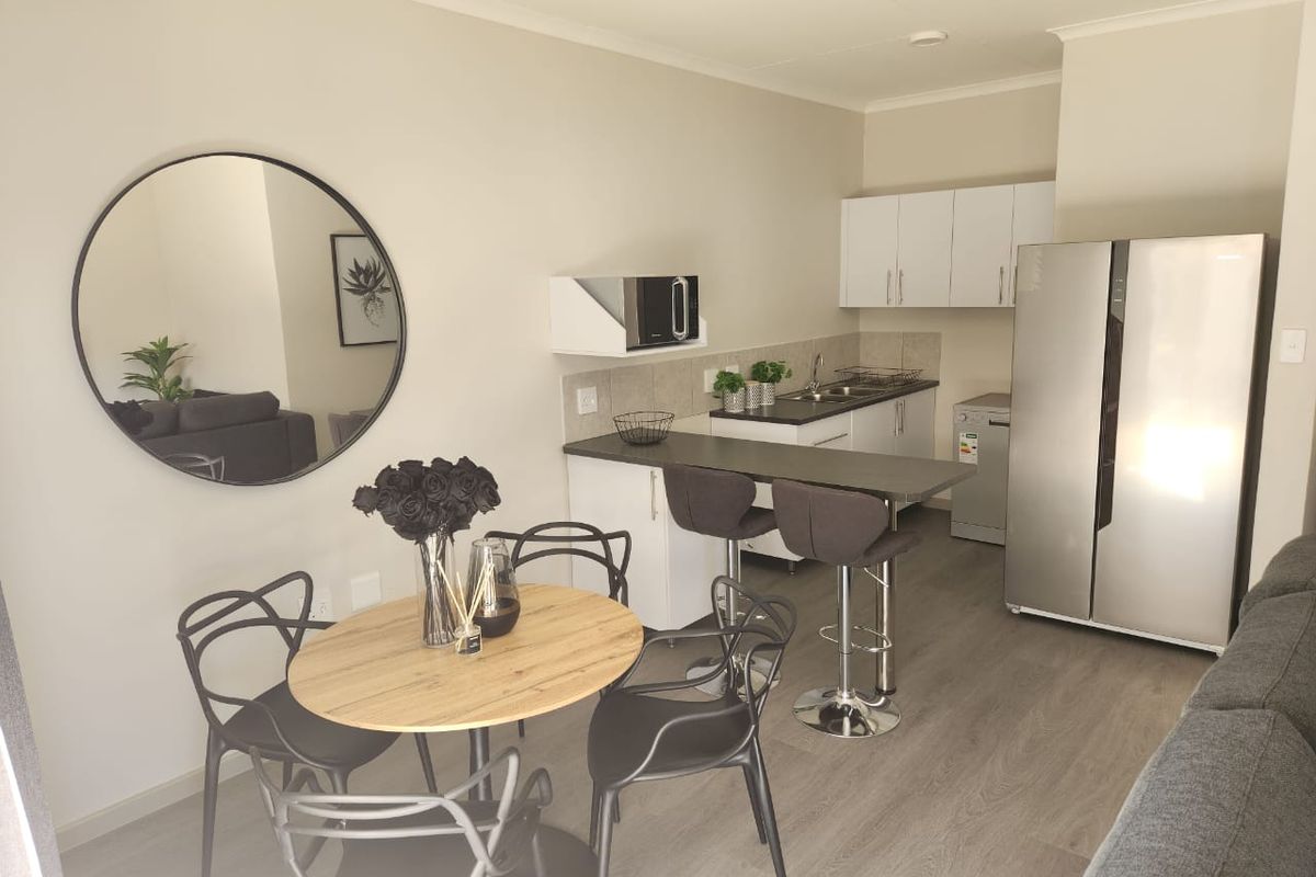 Modern open-plan kitchen and dining area featuring laminate flooring, sleek white cabinetry, and a functional breakfast bar for casual dining.