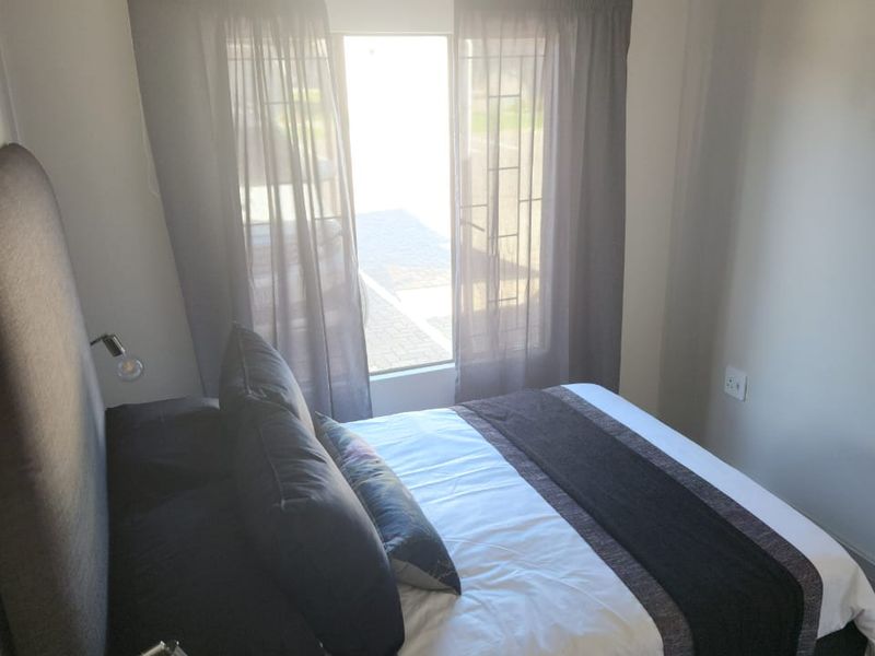 A compact bedroom featuring neutral wall tones, a window with curtains, and an electrical outlet.
