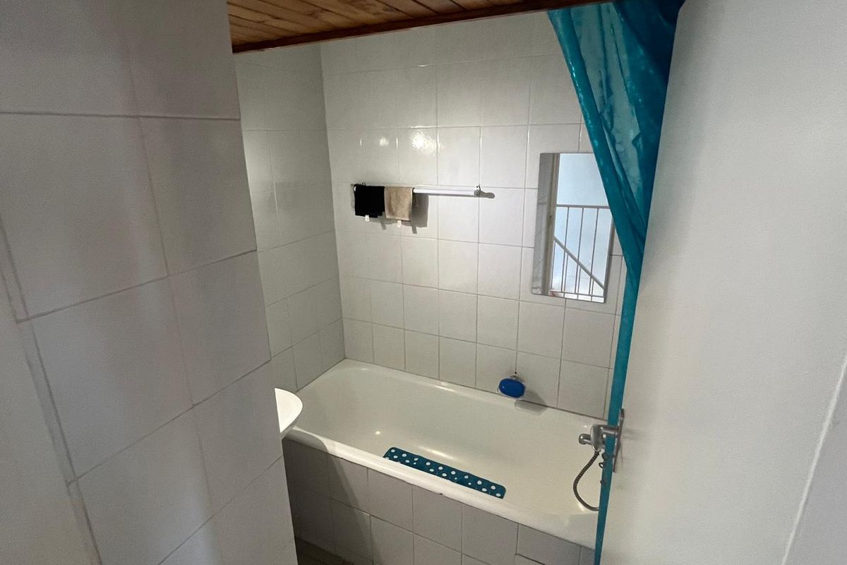 A functional bathroom featuring a bathtub with tiled surround, timber ceiling, and wall-mounted mirror.