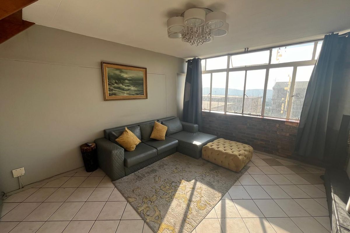 A living room featuring tiled flooring, exposed brick accents, and a large window providing natural light and an elevated view.