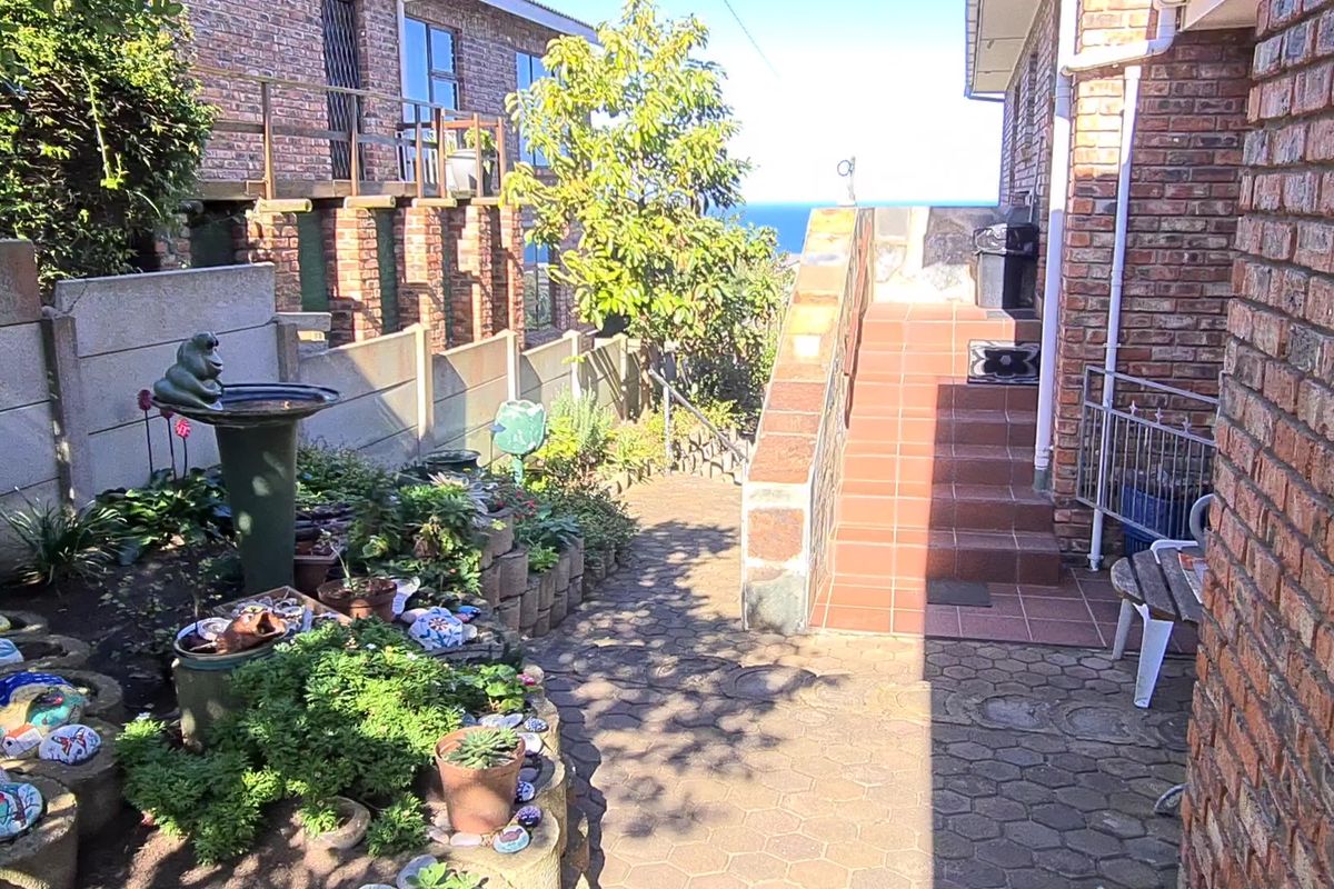 Rear exterior view featuring a brick facade, paved walkway, and tiled staircase leading to an elevated outdoor area with coastal views.