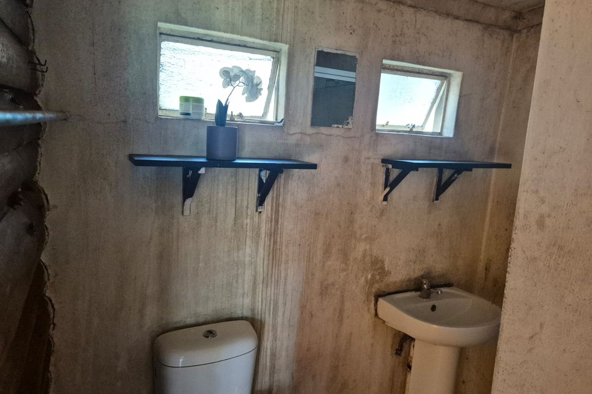 A small bathroom featuring a pedestal basin and toilet, requiring significant renovation and surface restoration to improve its condition.