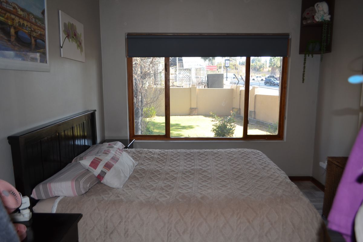 A bedroom featuring a large timber-framed window with a roller blind, offering a view of the exterior garden and boundary wall.