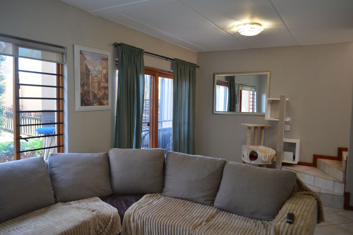 A living room featuring tiled flooring, sliding glass doors with security bars, and access to an internal staircase.
