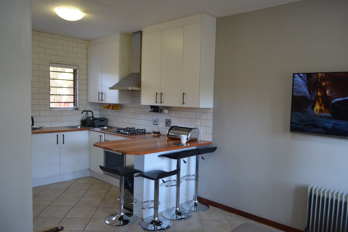 Compact kitchen featuring white cabinetry, wooden breakfast bar, gas hob, extractor fan, and subway tile backsplash with tiled flooring.