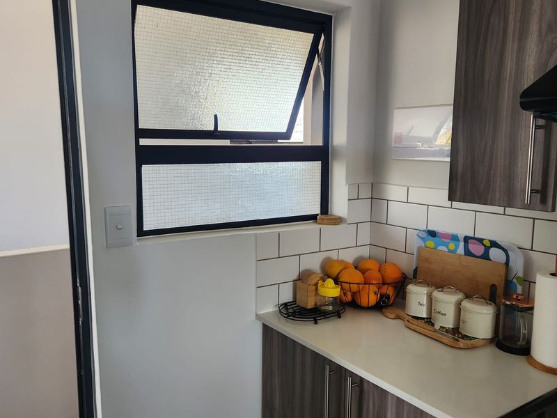 A modern kitchen area featuring dark wood-grain cabinetry, white subway tile backsplash, and a stone countertop with a functional top-hung window.
