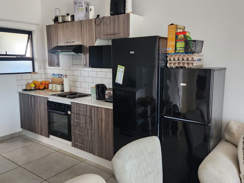 A compact kitchen featuring modern wood-grain cabinetry, a white subway tile backsplash, and integrated appliances including an oven and hob.