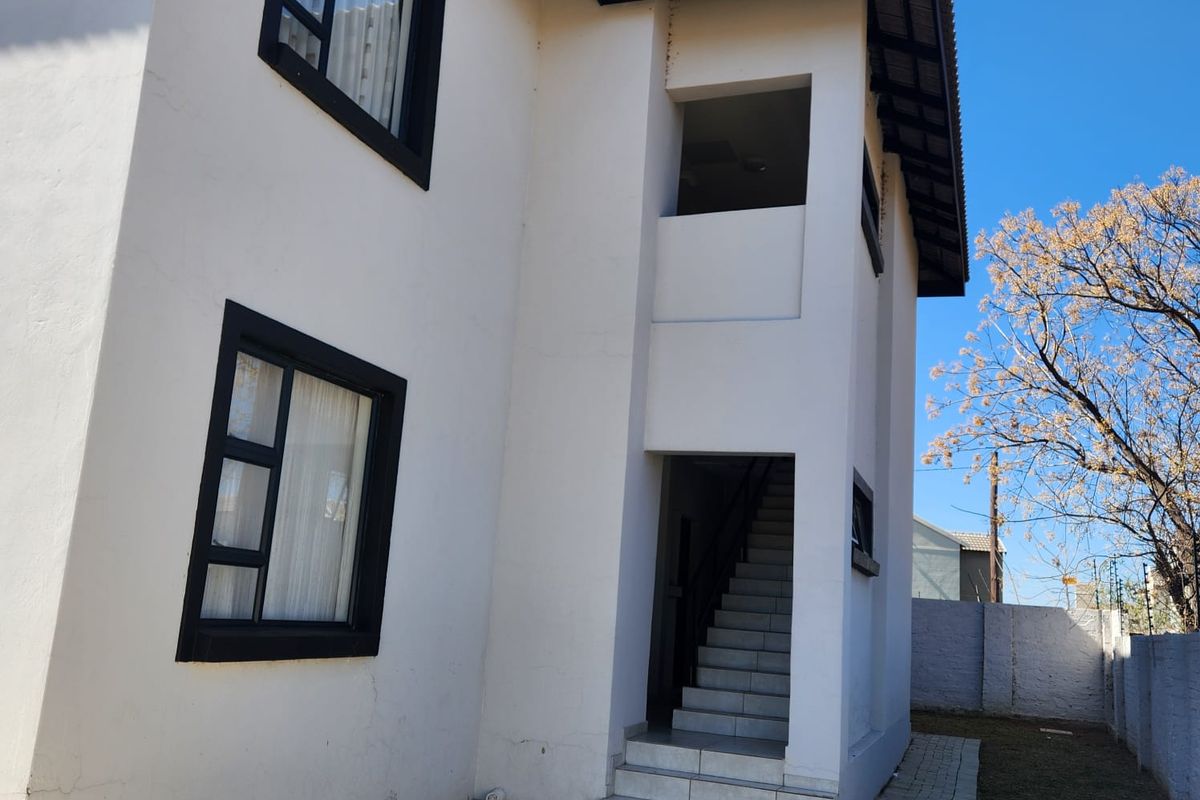 Rear view of a two-story apartment building featuring a tiled external staircase, paved walkway, and contrasting black window frames against white exterior walls.