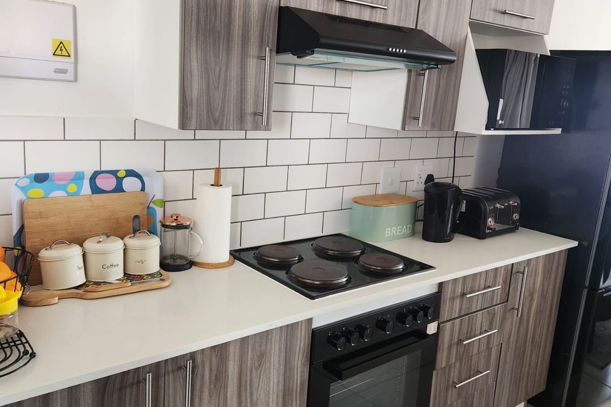 Modern kitchen featuring wood-grain cabinetry, white subway tile backsplash, stone countertops, and integrated electric cooking appliances.