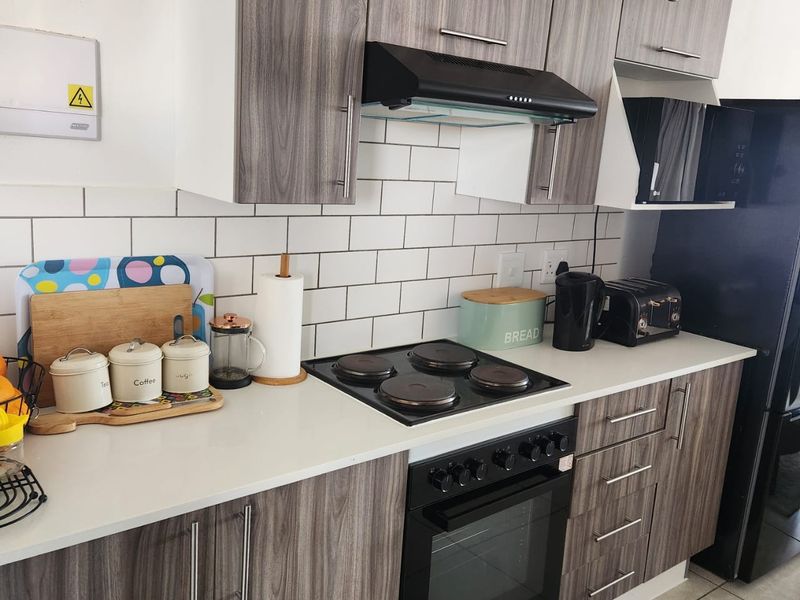 Modern kitchen featuring wood-grain cabinetry, white subway tile backsplash, stone countertops, and integrated electric cooking appliances.