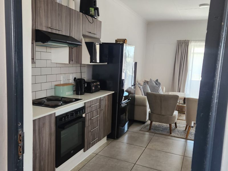 Open-plan kitchen and living area featuring modern wood-grain cabinetry, subway tile backsplash, built-in oven and hob, and neutral tiled flooring throughout.