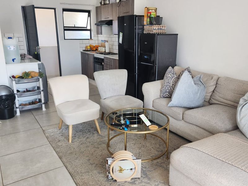 Open-plan living area featuring a compact kitchen with built-in cabinetry, oven, and hob, seamlessly connected to the lounge space with tiled flooring throughout.