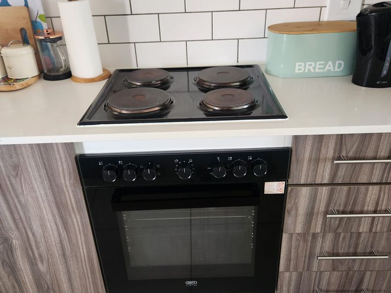 A kitchen area featuring a built-in Defy oven and electric hob, complemented by a white subway tile backsplash and modern wood-grain cabinetry.