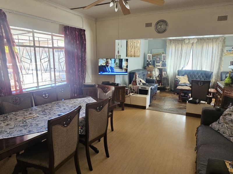 Open-plan living and dining area featuring laminate flooring, ceiling fan, and large windows with security bars, offering a functional and connected living space.