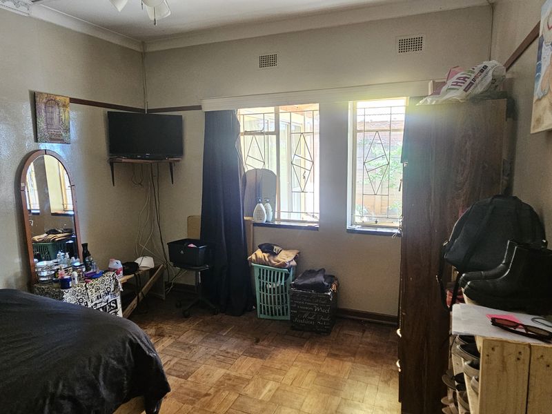 A bedroom featuring classic parquet flooring, decorative picture rails, and security bars on the windows, offering a functional space with potential for cosmetic updates.