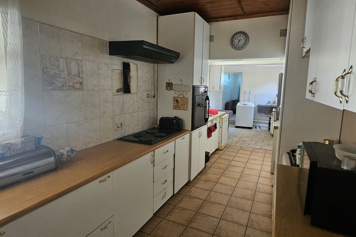 A functional kitchen featuring built-in cabinetry, an electric hob with extractor fan, and tiled flooring, leading through to a secondary utility or laundry area.