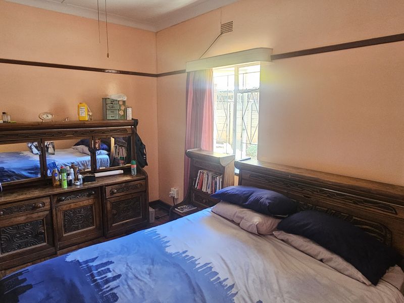 A bedroom featuring a classic picture rail, ceiling ventilation, and a window fitted with security bars.
