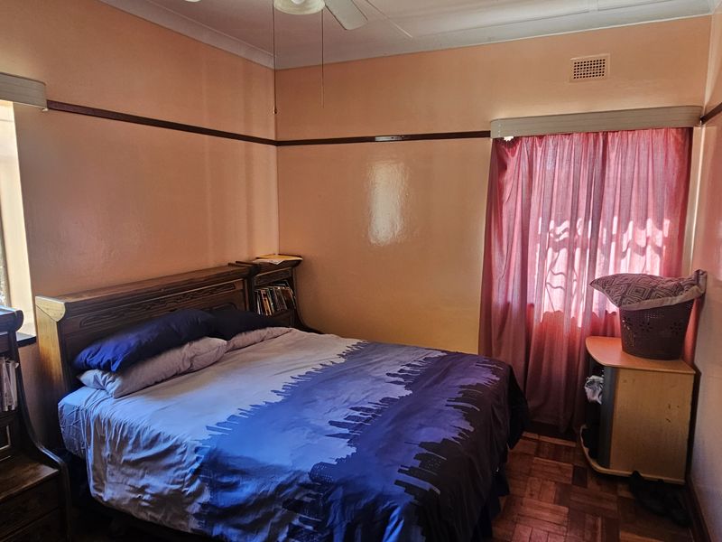 A bedroom featuring classic parquet flooring, a ceiling fan, and built-in storage, currently requiring cosmetic updates to the wall finishes.
